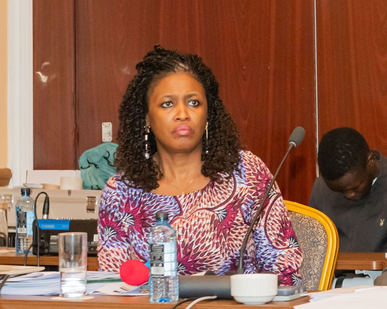 A delegate at the table with meeting papers, a microphone and a glass of water.