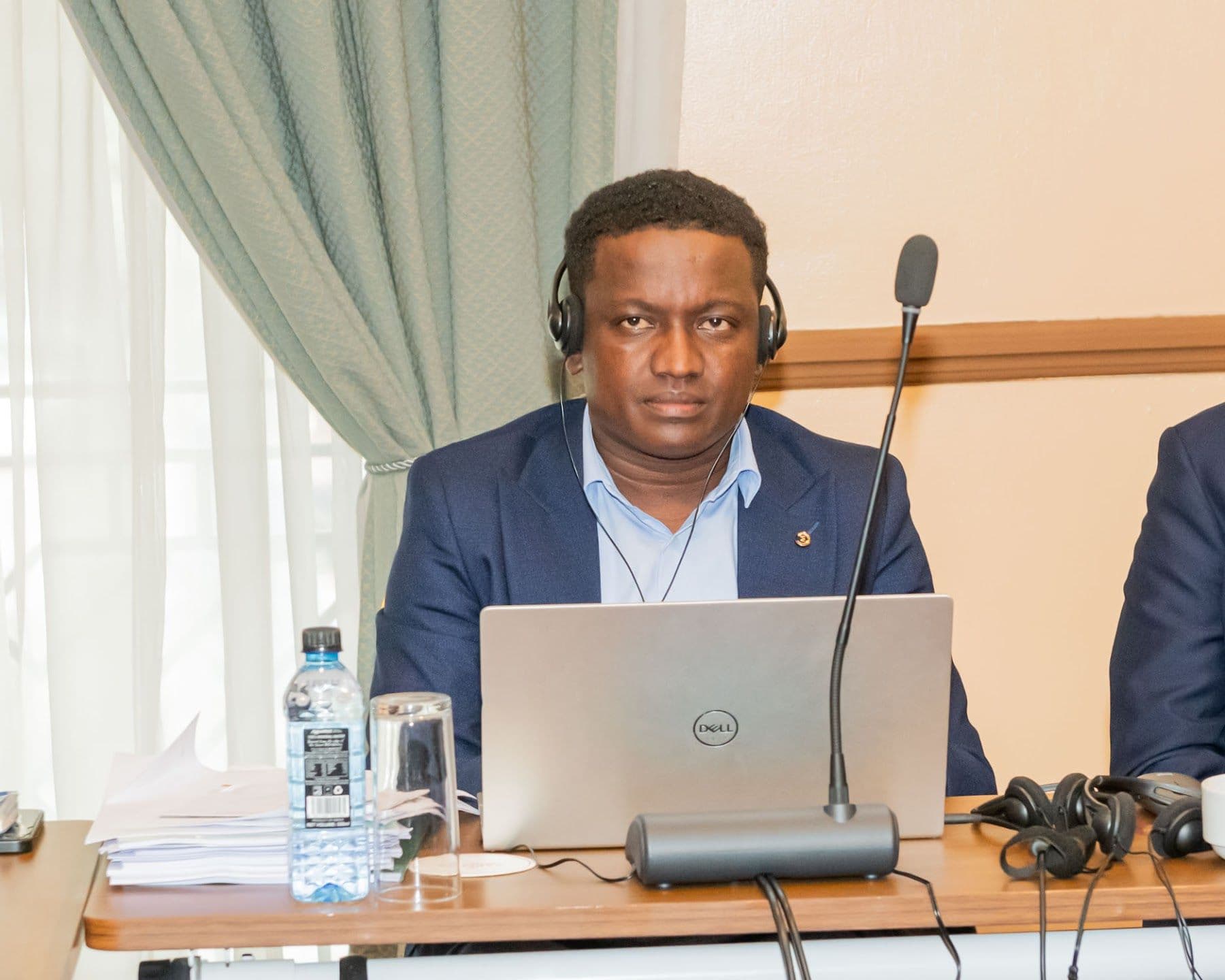 A delegate seated by the window follows the session with an interpretation headset and laptop.