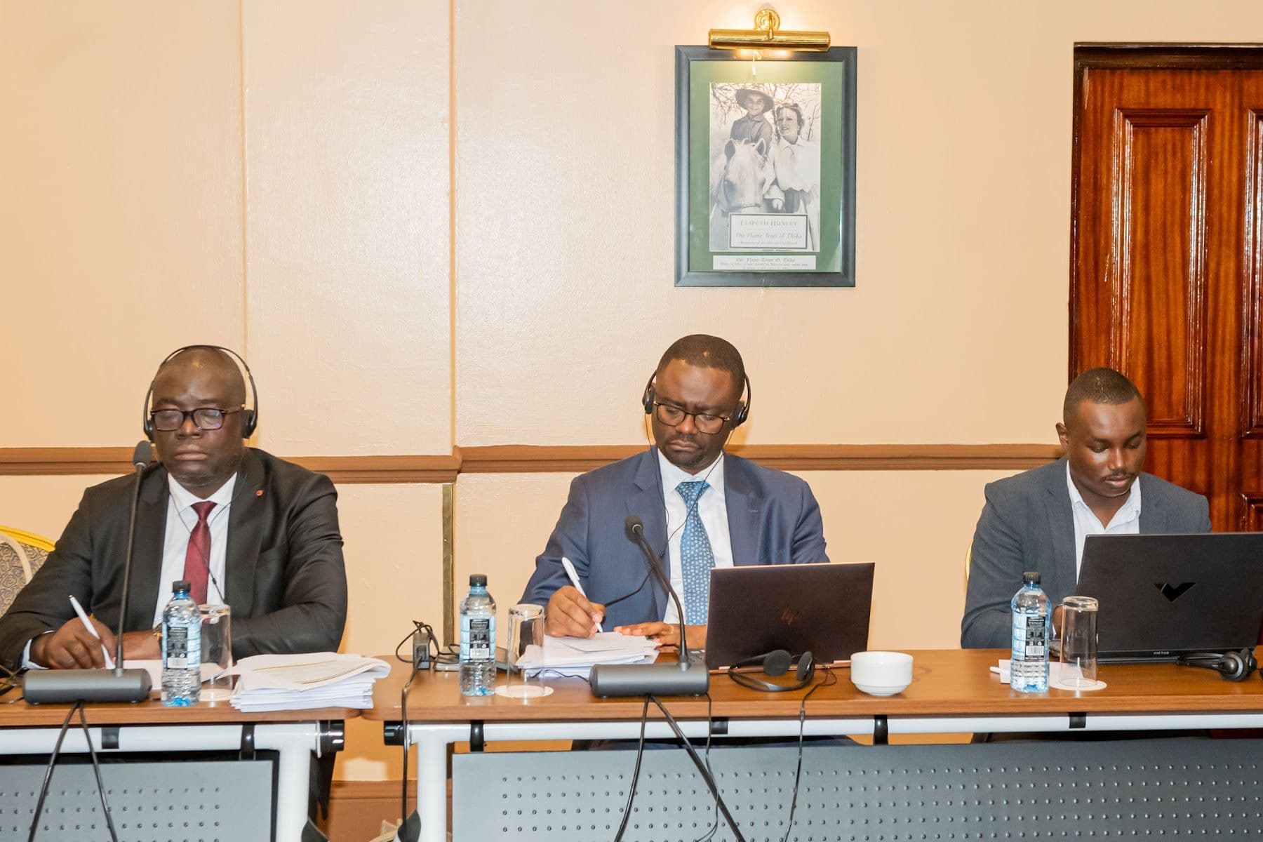 Three delegates taking notes at the meeting table, laptops and meeting papers in front of them.