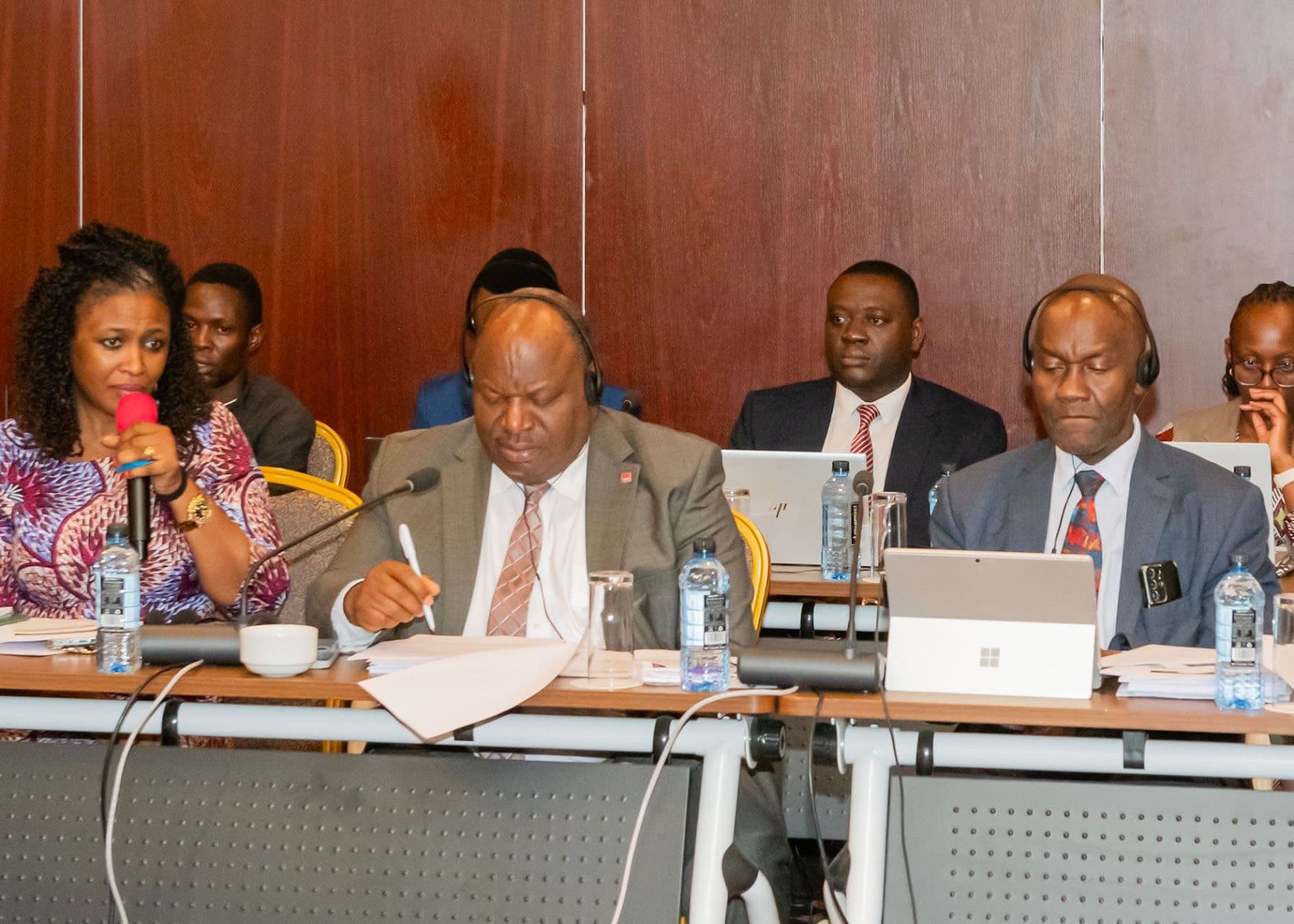 Executive Committee members seated along the conference table, one speaking into a handheld microphone.