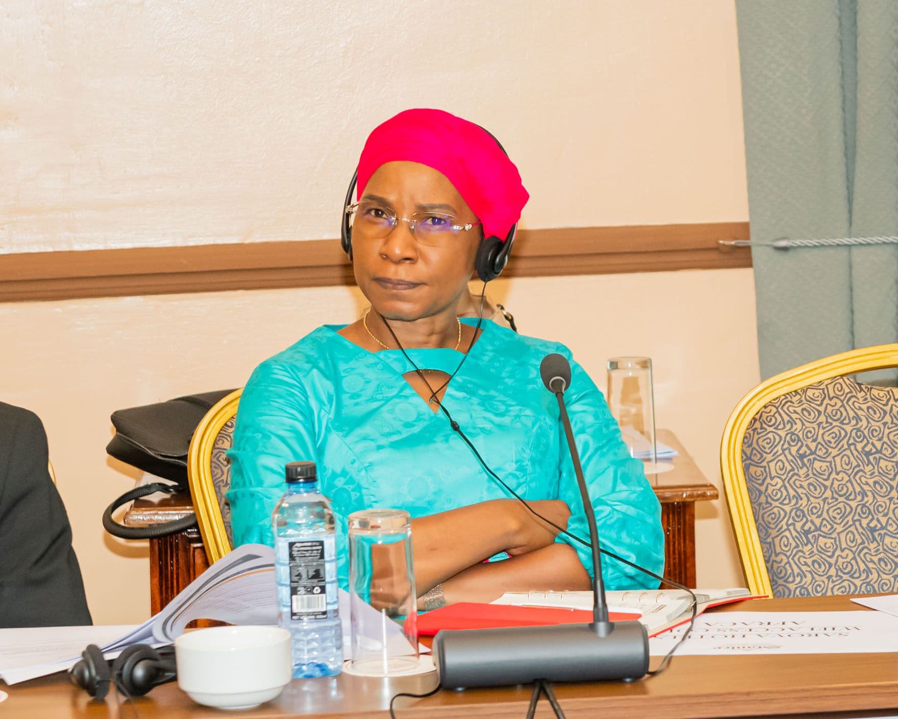 A delegate in a bright headwrap listens through an interpretation headset, meeting file open on the table.